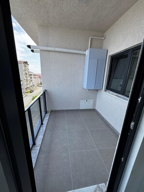 Ein Balkon mit grauen Fliesen, einem Fenster und einem weißen Schrank.