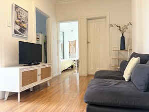 A modern living room with a flat-screen TV, a grey sofa, a white entertainment unit, and a wooden floor. - Potts Point Cosy 1BR | Walk to CBD, Train, Cafes & Harbour! (Potts Point)