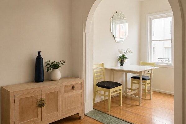 A room with a wooden cabinet, a table, two chairs, a vase with a plant, and a mirror on the wall. - Potts Point Cosy 1BR | Walk to CBD, Train, Cafes & Harbour! (Potts Point)