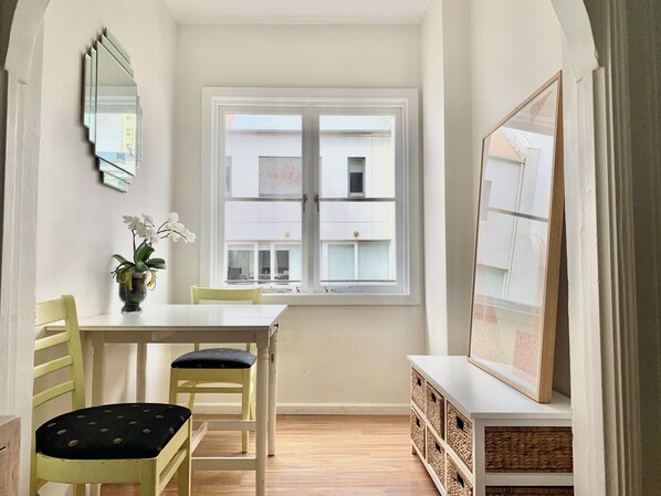 A room with a dining table, chairs, a vase with flowers, a window, and a cabinet with baskets. - Potts Point Cosy 1BR | Walk to CBD, Train, Cafes & Harbour! (Potts Point)