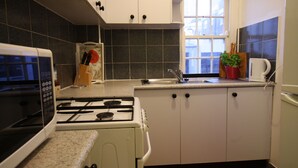 Eine Küche mit weißen Schränken, einem Herd, einer Mikrowelle, einem Spülbecken und einem Fenster.