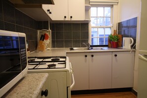 A kitchen with white cabinets, a stove, a microwave, a sink, and a window. - Potts Point Cosy 1BR | Walk to CBD, Train, Cafes & Harbour! (Potts Point)