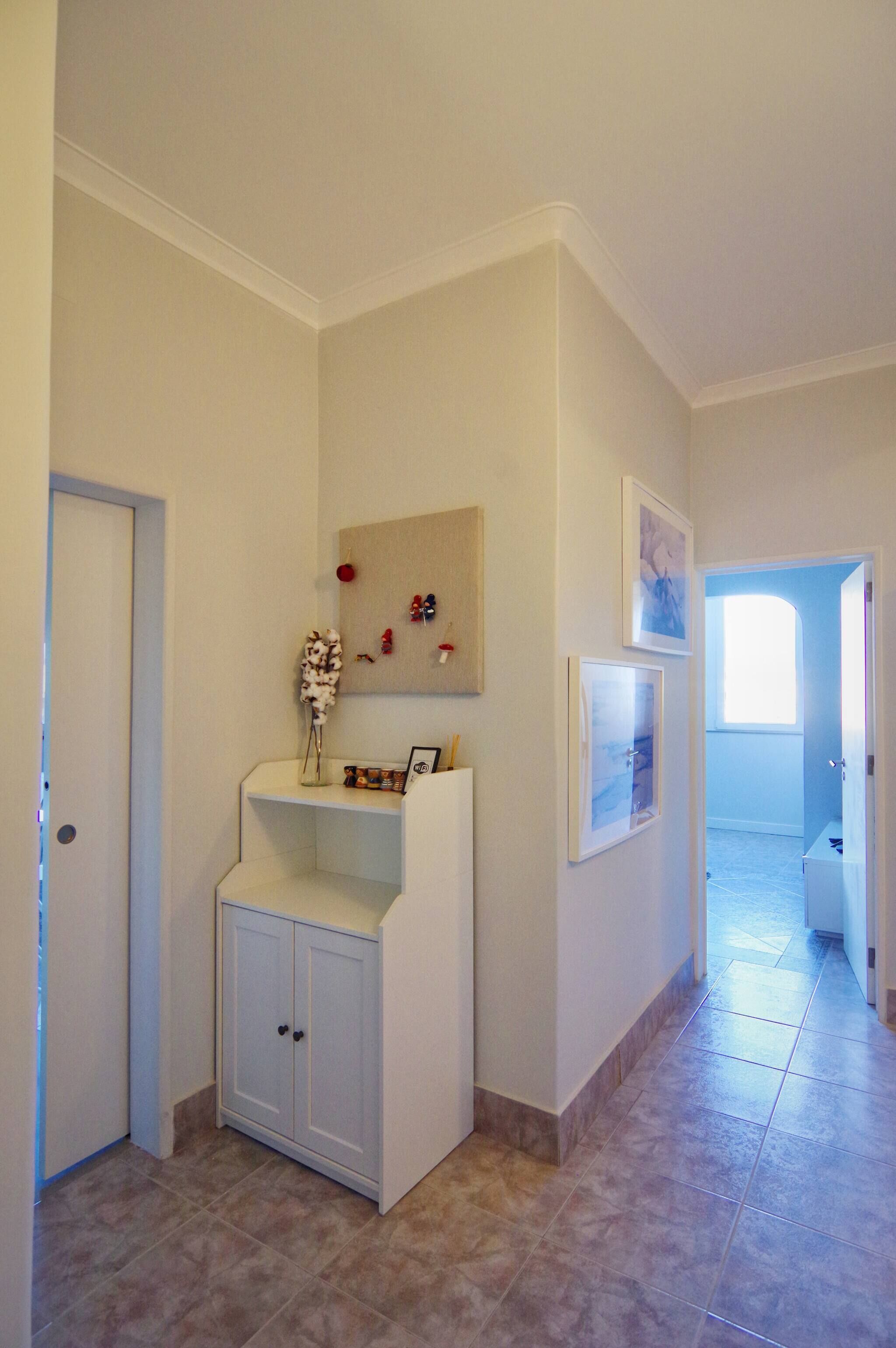 A hallway with a white cabinet, a door, and a wall with framed pictures.