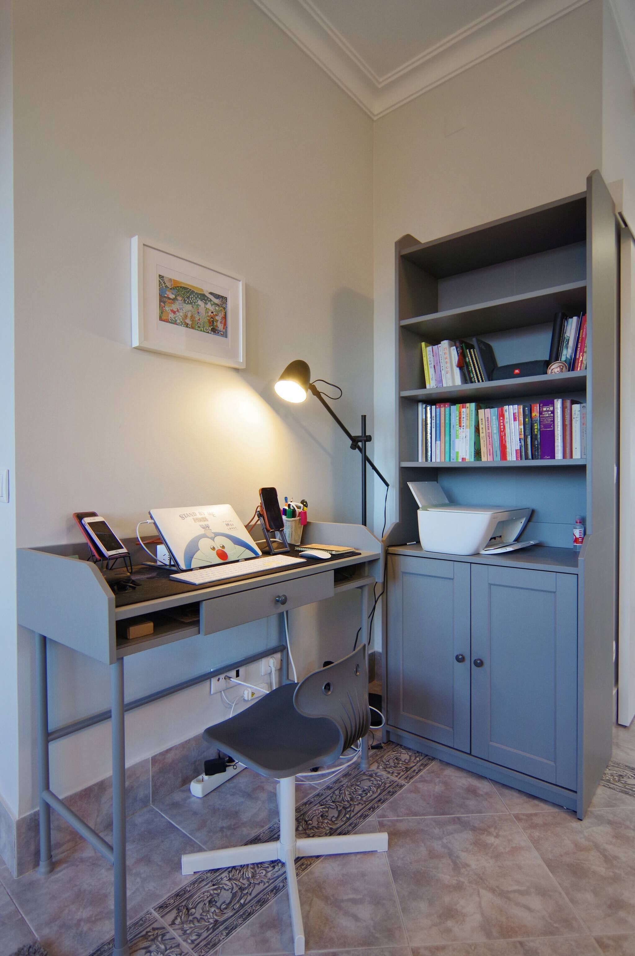 A study area with a desk, chair, lamp, bookshelf, and a framed picture on the wall.
