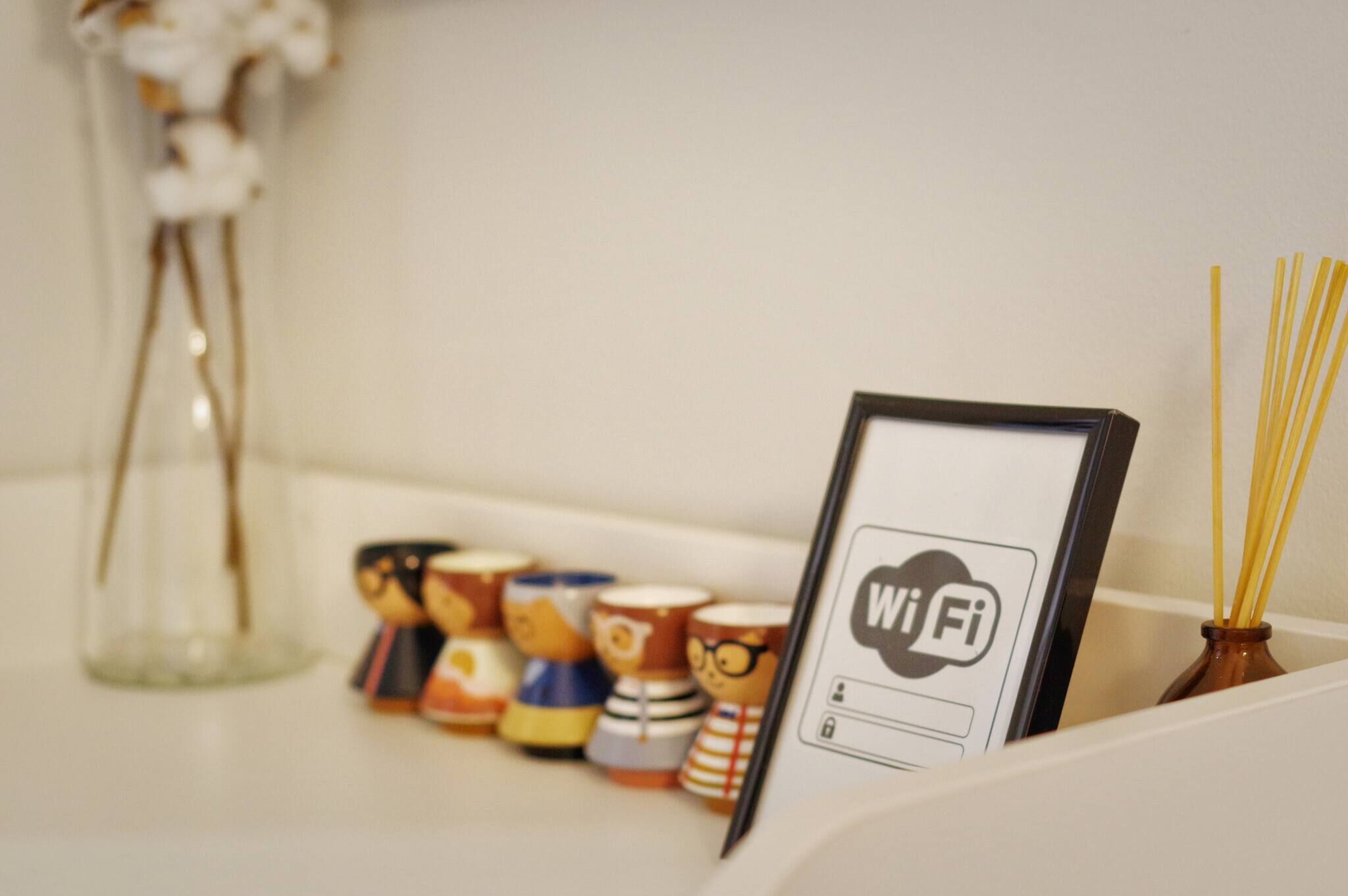 Ein gerahmtes WLAN-Symbol, eine Reihe Holzschnitzfiguren und eine Vase mit Schilf.