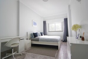 A bedroom with a bed, a desk, a chair, a nightstand, a window with curtains, and a vase with flowers. - Entire Cascais New Mordern Apartment-3 Bedrooms (Cascais)
