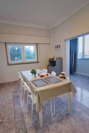 A dining area with a table, chairs, a small plant, and a window with curtains. - Entire Cascais New Mordern Apartment-3 Bedrooms (Cascais)