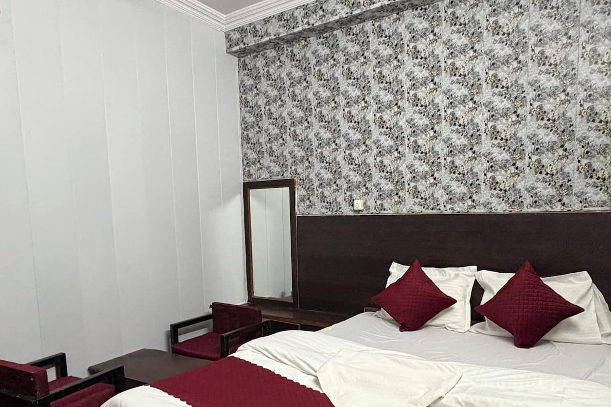 Quarto com uma cama grande, um ventilador de teto, uma mesa de cabeceira de madeira, um espelho e uma cadeira.