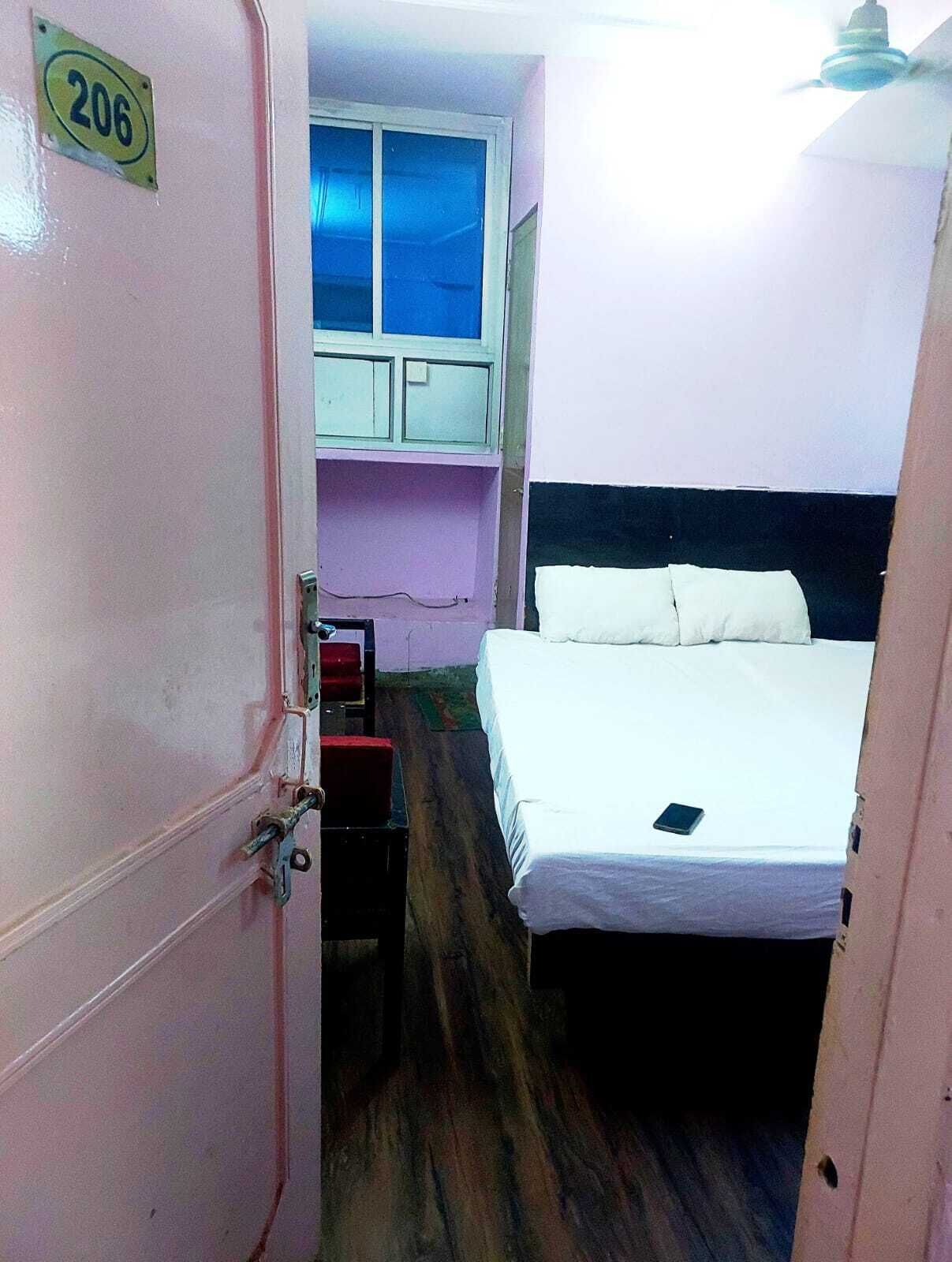A small, narrow room with a bed, a window, a door, and a small table.
