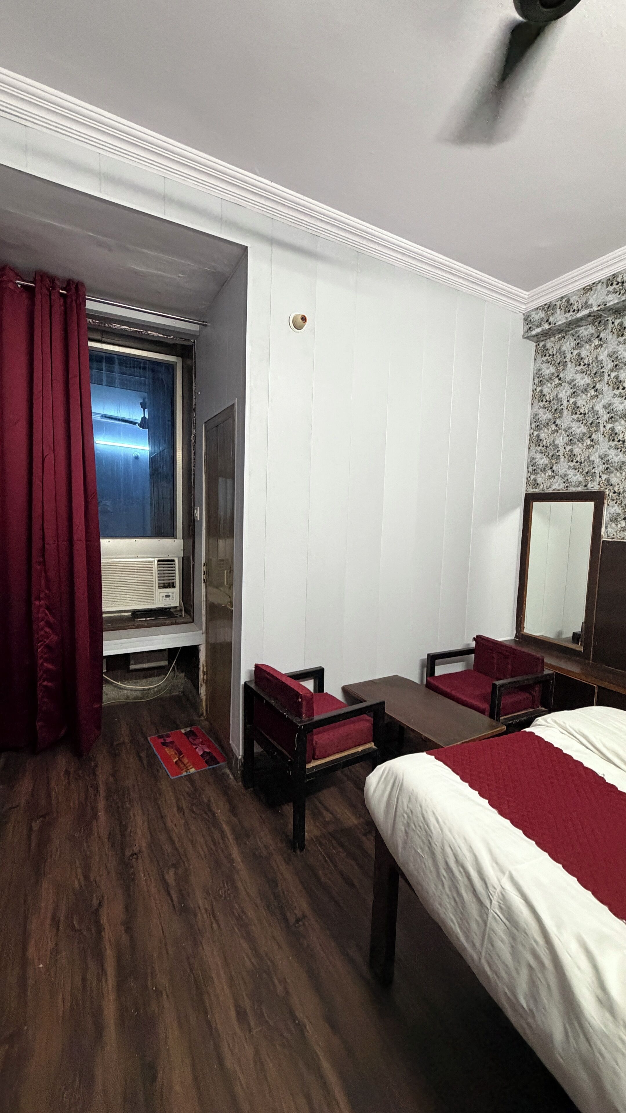 Habitación de hotel con cama, escritorio, silla, ventana con cortinas y ventilador de techo.