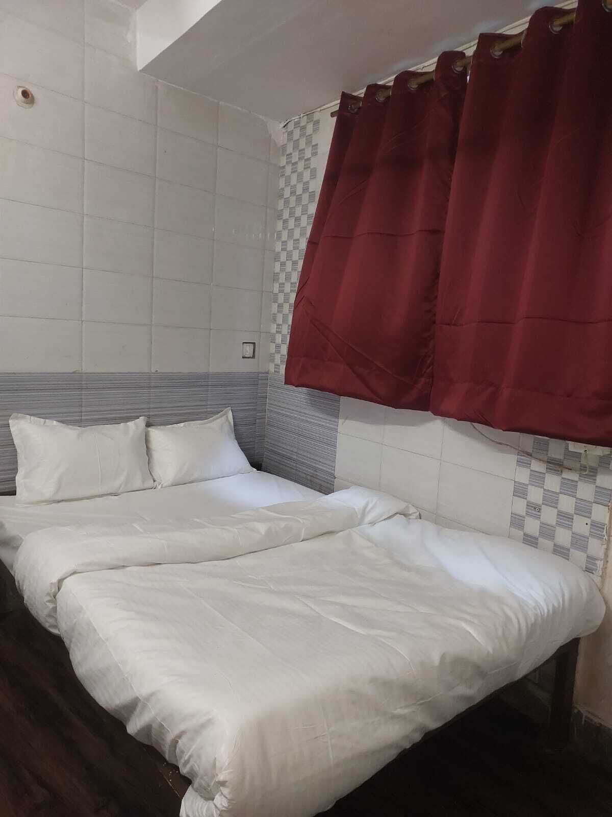 A double bed with white bedding, a checkered wall pattern, and a red curtain.
