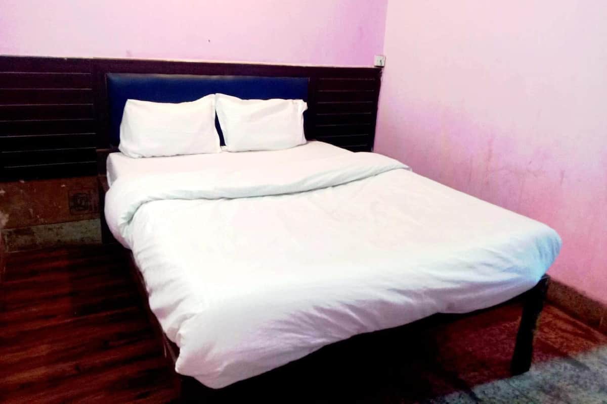 Uma cama de solteiro com cabeceira de madeira, roupa de cama branca e uma parede lisa.