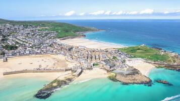 An aerial view of a coastal town with a beach, rocky coastline, and a mix of residential and commercial buildings.