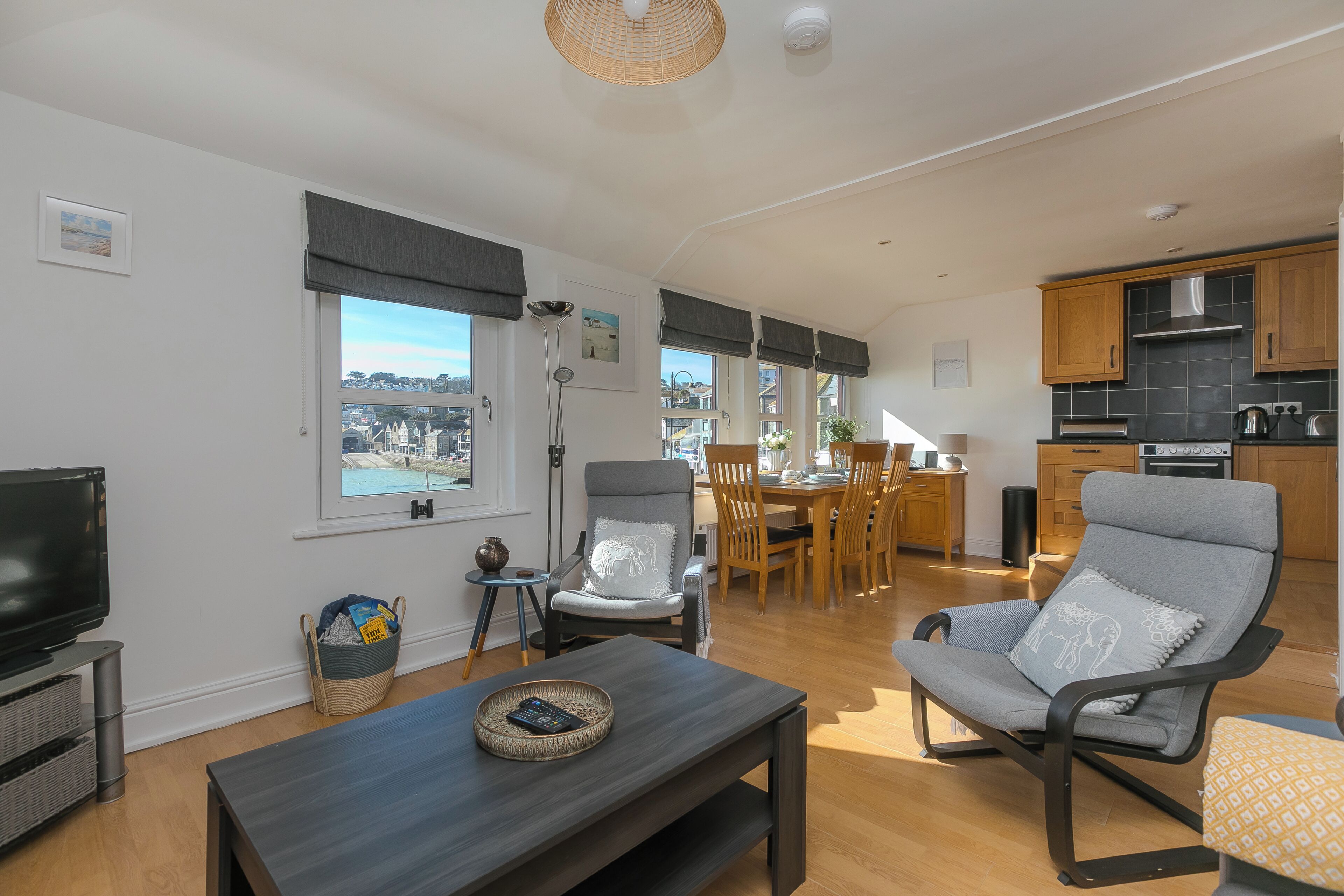 A modern living room with a TV, a dining area with a table and chairs, a kitchen with wooden cabinets, and a view of the city.