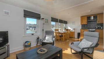 A modern living room with a TV, a dining area with a table and chairs, a kitchen with wooden cabinets, and a view of the city.