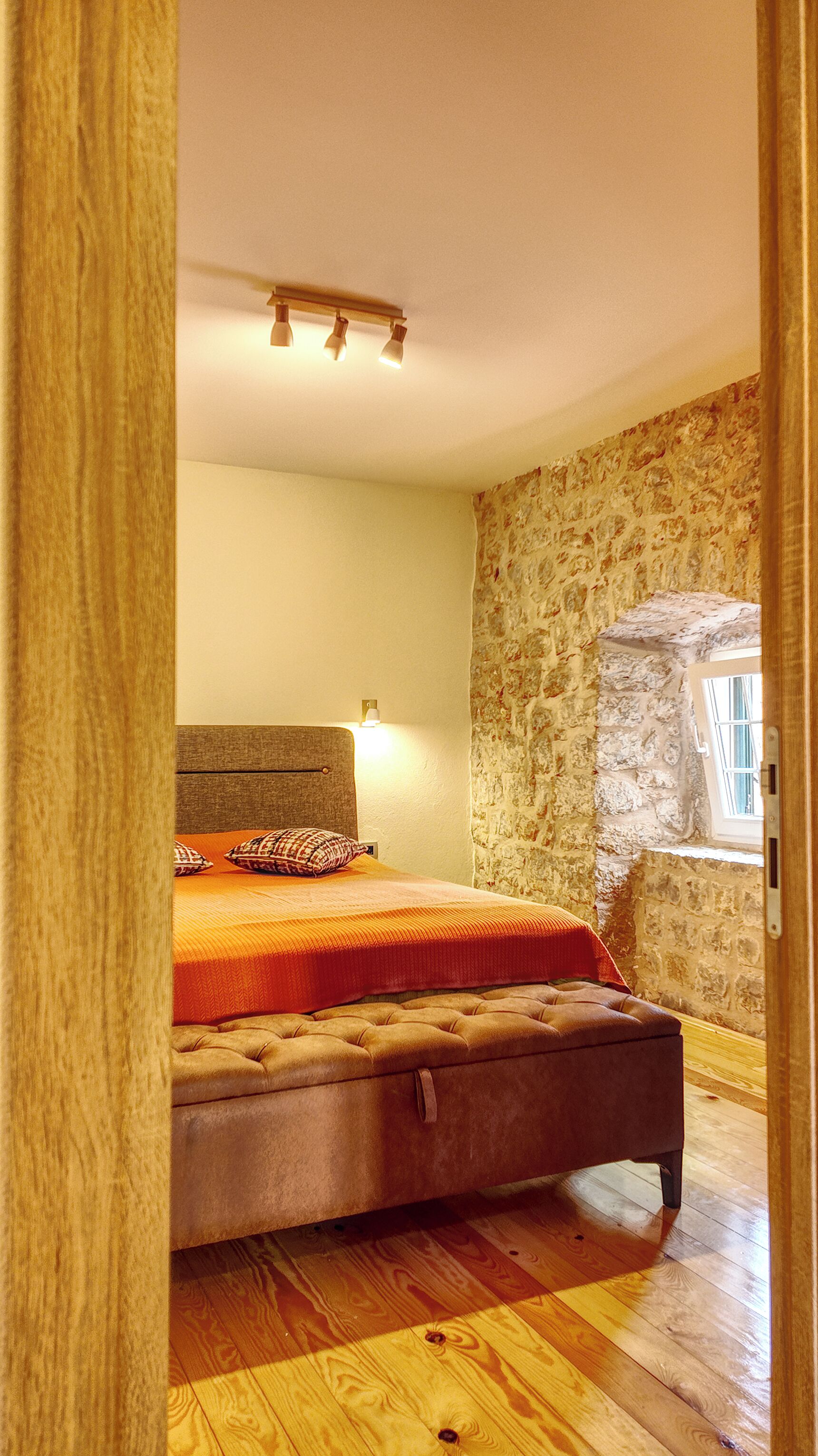 A bedroom with a bed, a stone wall, a window, and a wooden floor.