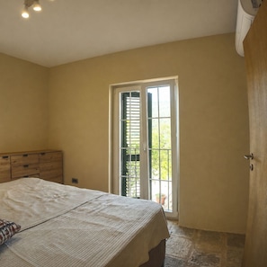 A bedroom with a bed, a wooden dresser, a sliding glass door, and a stone floor.