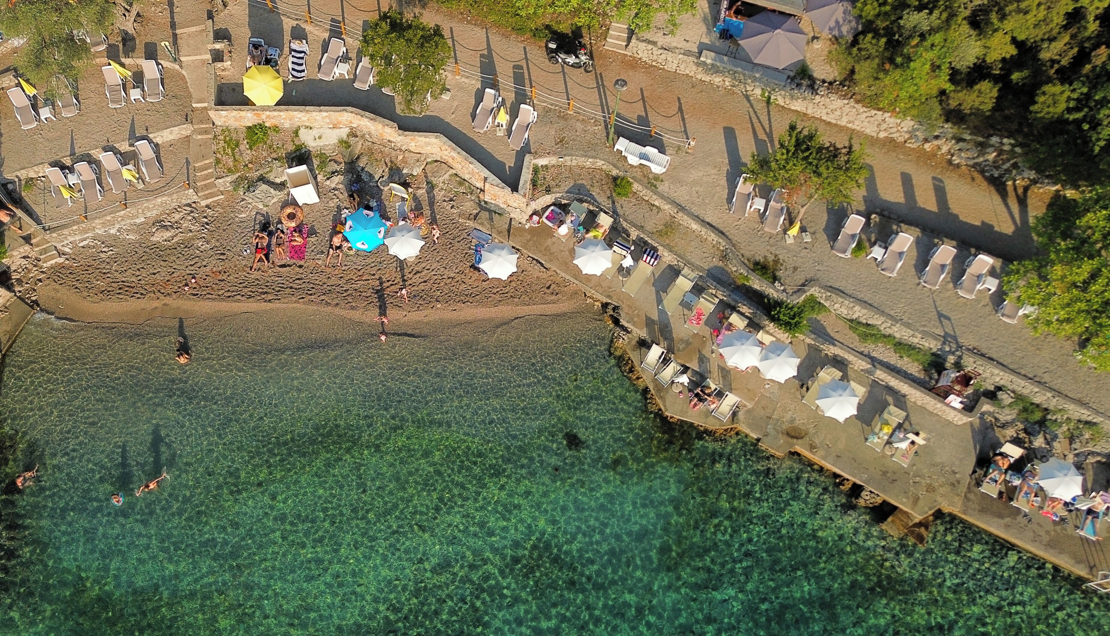 Vista aérea de una playa con agua cristalina, sillas de playa, sombrillas y algunas personas.