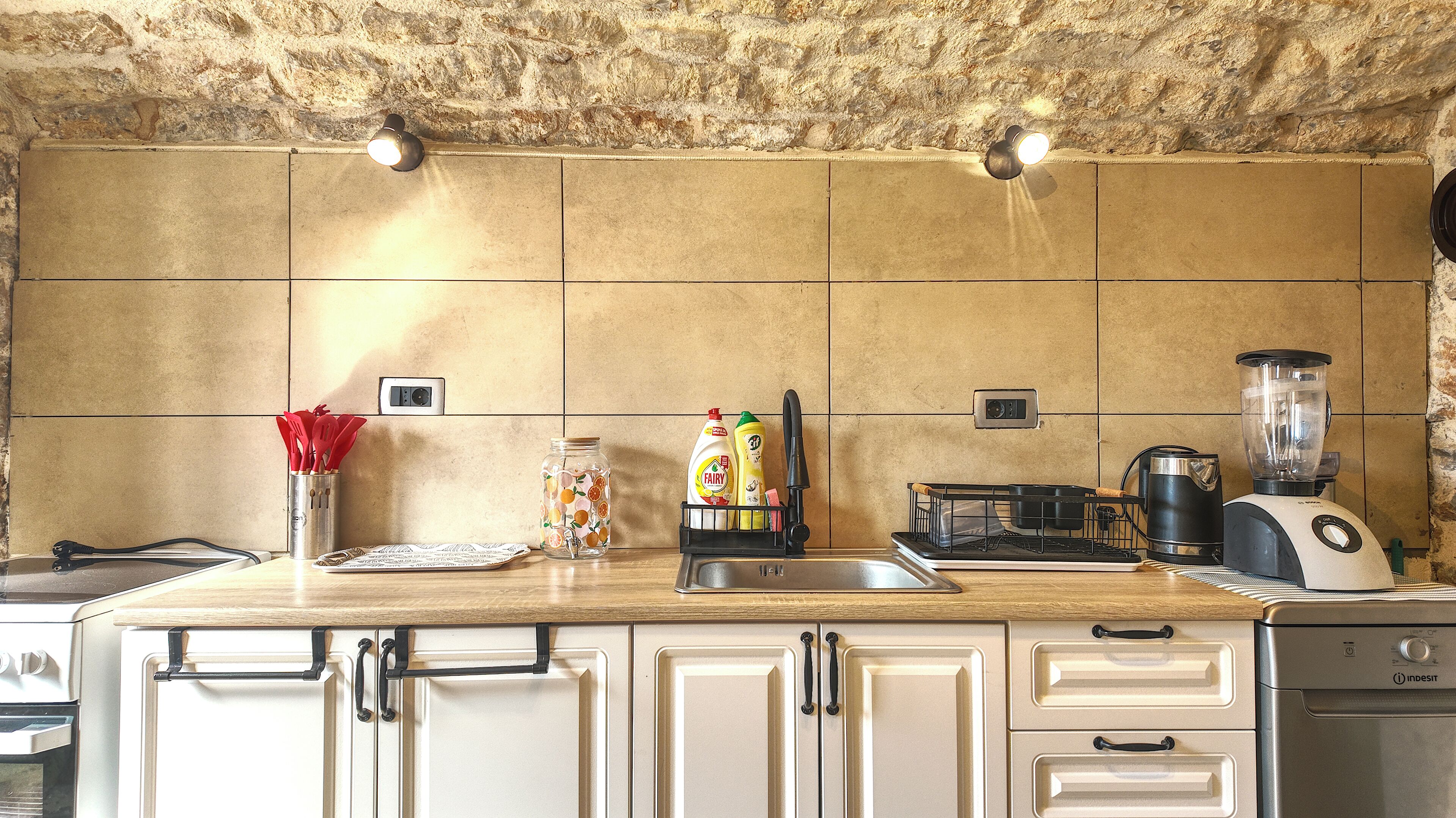 A kitchen with a stone wall, a countertop with various appliances, and cabinets.