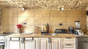 A kitchen with a stone wall, a countertop with various appliances, and cabinets. - A fantastic four-room house in Luštica, free sunbeds on Mirišta beach. (Herceg Novi)