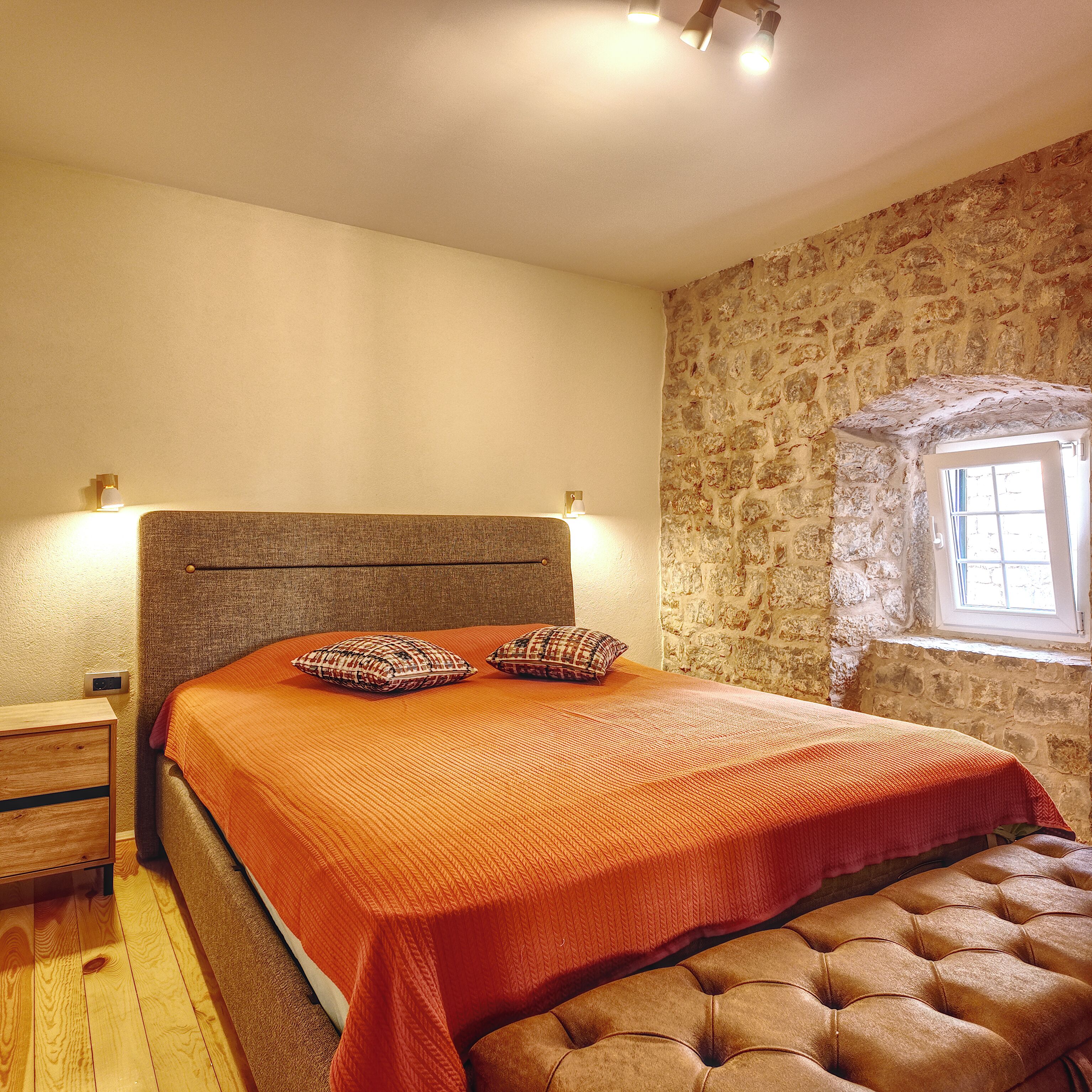 Ein Schlafzimmer mit einem Bett, einem Nachttisch, einem Fenster und einer Steinwand.