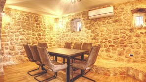 A stone-walled room with a wooden table and leather chairs, an air conditioning unit, and a small window.