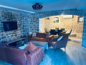 A stone-walled room with a TV, a sofa, a coffee table, and a dining area with chairs and a table.