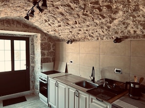 A kitchen with stone walls, a tiled backsplash, a sink, and a stove.