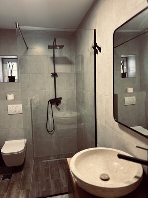 Et moderne badeværelse med et glasbadeværelsesafskærmning, et hvidt toilet og en rund vask med et spejl over.