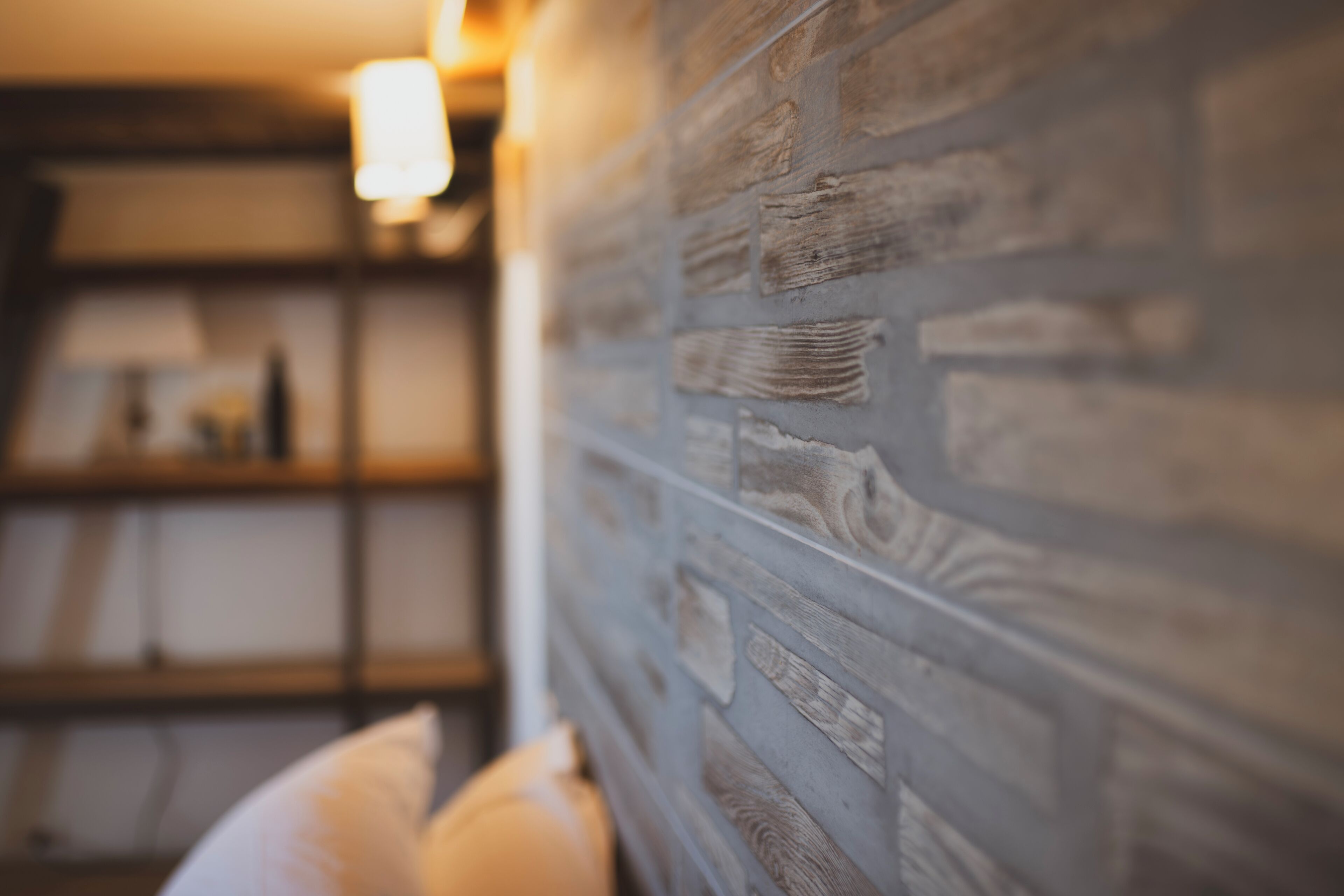 A room with a brick-patterned wall, a shelf with items, and a white pillow.