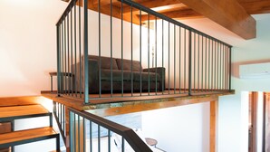 Eine Holztreppe mit Metallgeländer führt zu einem Schlafzimmer auf einem Dachboden, inklusive Bett und Sofa.
