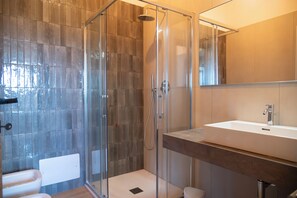 Un bany modern amb una cabina de dutxa de vidre, un lavabo blanc i un mirall gran.