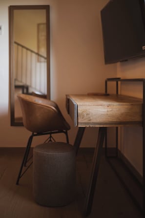 Habitació amb escriptori de fusta, una cadira, televisió, mirall i un petit otomà.