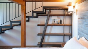 Eine Treppe mit Holzsitzstufen und Metallgeländern, ein an der Wand befestigtes Regal mit Dekorationen sowie ein Bett mit weißer Bettwäsche.