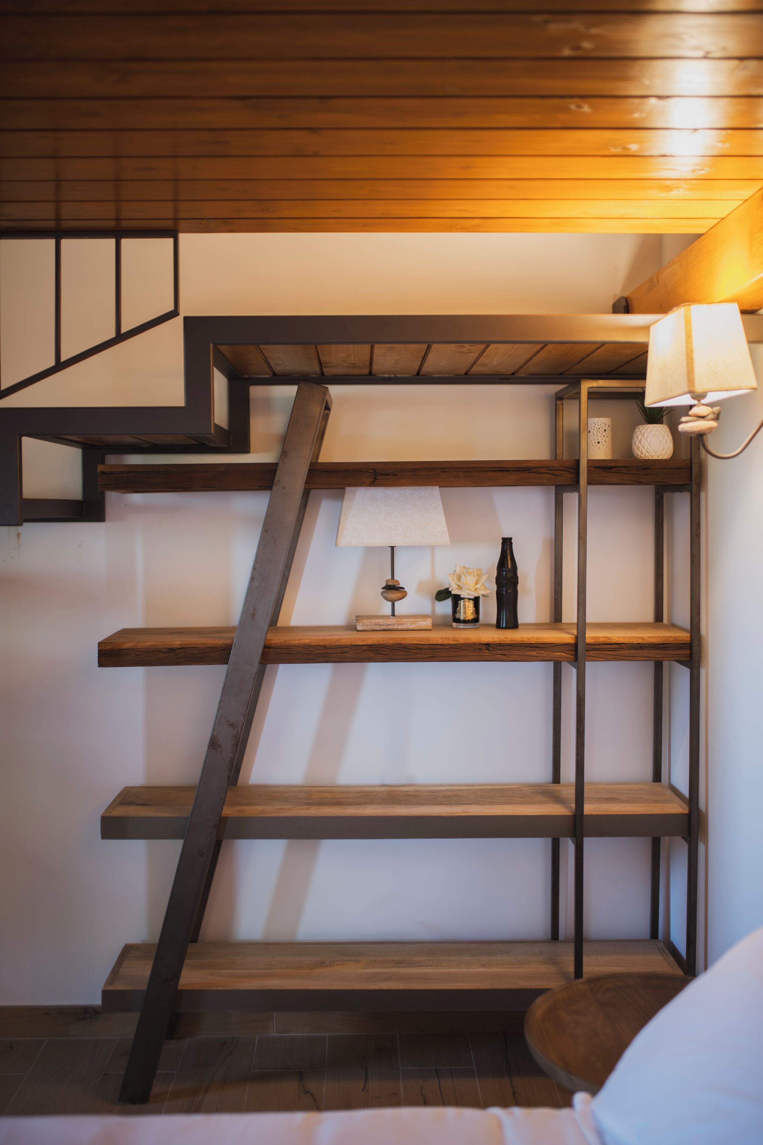 Een trap met houten treden en metalen leuningen, leidend naar een plateau met planken en een lamp.