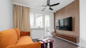 Un soggiorno moderno con divano, tavolino, TV a parete e ventilatore a soffitto.