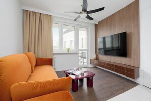 Ein modernes Wohnzimmer mit einer Couch, einem Couchtisch, einem an der Wand montierten Fernseher und einem Deckenventilator.