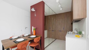 Una cucina moderna con mobili in legno, un piano di lavoro bianco e un'area pranzo con tavolo in legno e sedie arancioni.