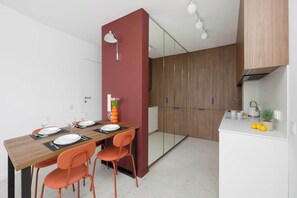Eine moderne Küche mit Holzschränken, einer weißen Arbeitsplatte und einem Essbereich mit Holztisch und orangefarbenen Stühlen.
