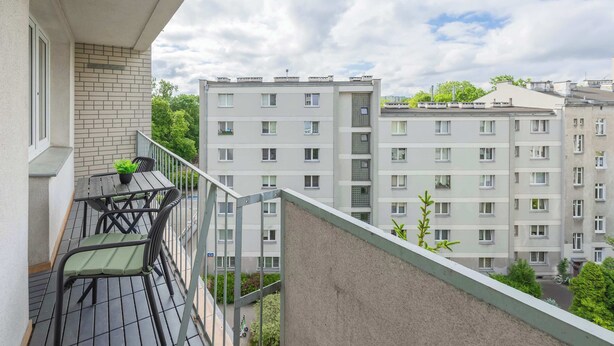 Un balcone con tavolo e sedie, una pianta in vaso e vista su edifici residenziali a più piani.