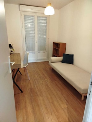 Una habitación pequeña y bien iluminada con suelo de madera, un sofá blanco, una mesita de madera y una silla.