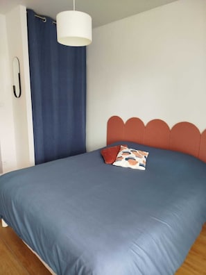 Una cama con colchón azul, lámpara colgante blanca y cortina azul.