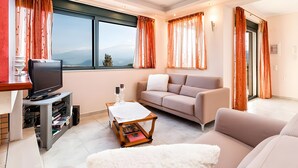 A living room with a television, sofa, coffee table, and a view of the mountains through large windows. - Villa Renata with Private Pool, Mountain View, Wi-Fi and Air Conditioning (Aptera)