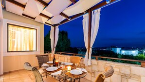An outdoor dining area with a table set for two, a bottle of wine, and a candle on a terrace overlooking a cityscape at night. - Villa Renata with Private Pool, Mountain View, Wi-Fi and Air Conditioning (Aptera)