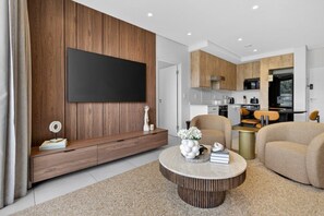 Ein modernes Wohnzimmer mit Flachbildfernseher, Holzwandverkleidung, rundem Couchtisch und Sofa.