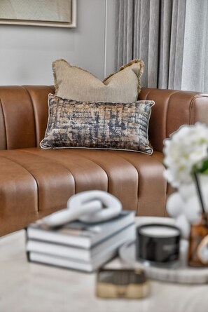 Ein braunes Ledersofa mit einem gemusterten Kissen und einem Stapel Bücher auf einem Tisch.