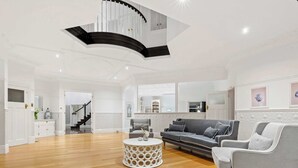 A spacious living room with a staircase, a round coffee table, and a grey sofa. - Kirinaran Manor | Pool & Games Room (Frankston South)