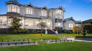 A large, multi-story house with a prominent tower, a well-maintained lawn, and a fountain. - Kirinaran Manor | Pool & Games Room (Frankston South)