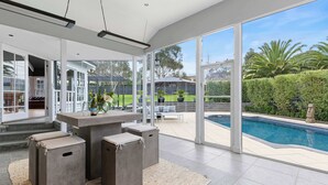 A modern outdoor living area with a pool, large windows, and a patio with seating. - Kirinaran Manor | Pool & Games Room (Frankston South)