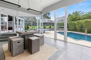 A modern outdoor living area with a pool, large windows, and a patio with seating. - Kirinaran Manor Pool & Bar Room (Frankston South)